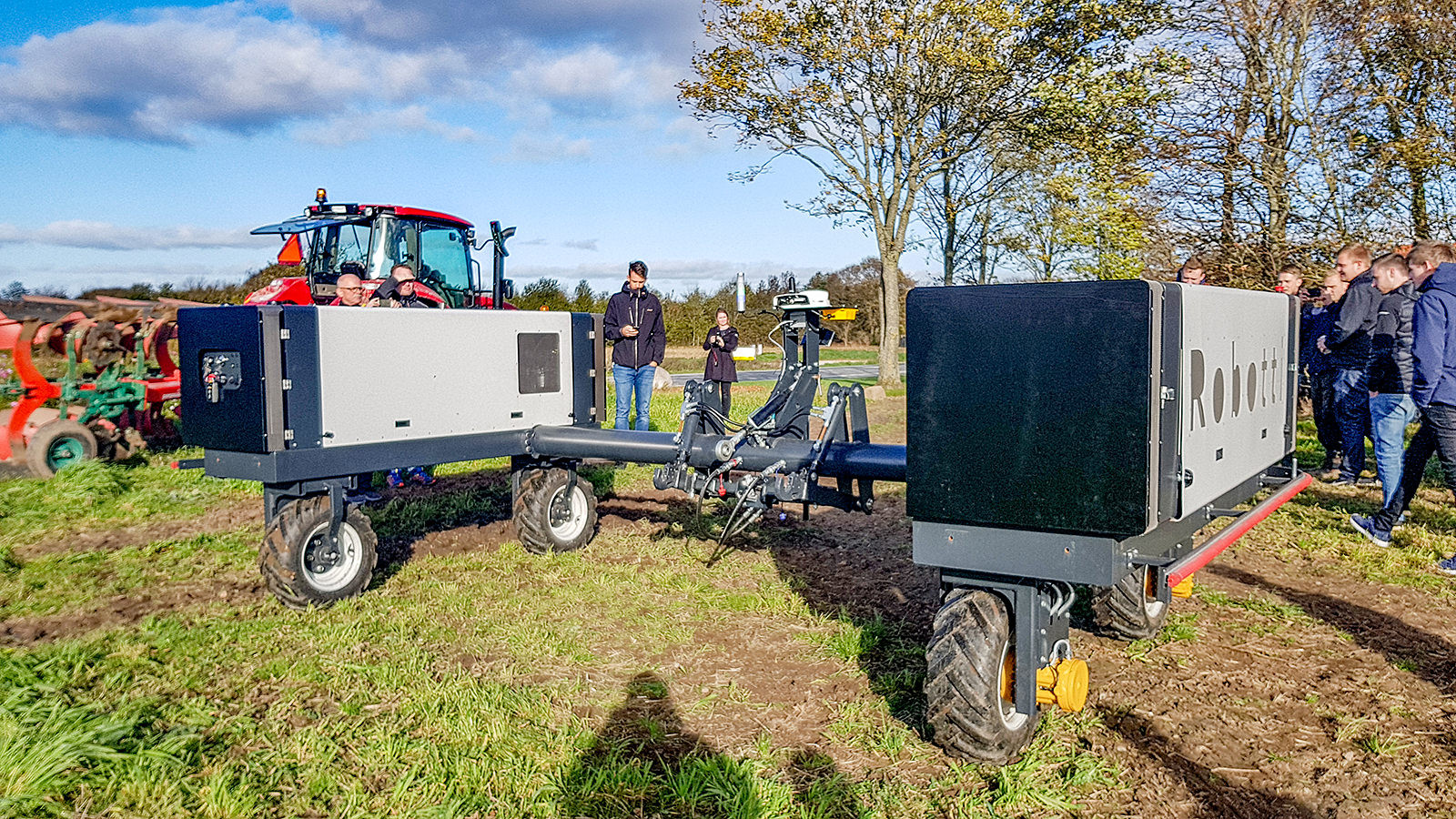 Landbrugselever går rundt om den firhjulede markrobot Robotti, der står på en mark ved siden af en traktor